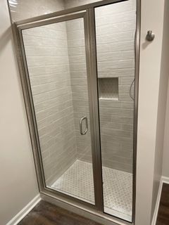 Glass shower enclosure with gray tile walls and white floor.