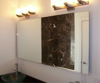 Bathroom mirror over a dark countertop with a glass bowl sink. Marble wall accent and light fixtures.