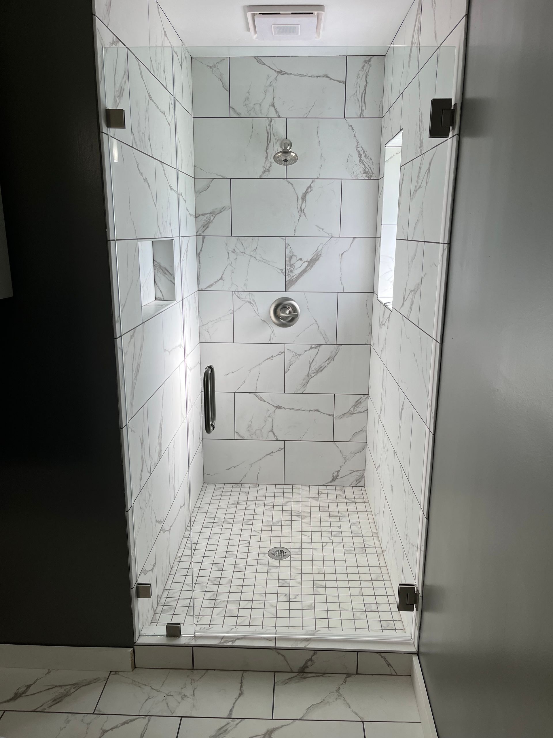 Modern shower with white marble tile and glass doors.