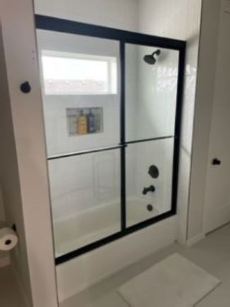 Black-framed sliding glass shower door in a white bathroom, with a built-in shelf and shower fixtures.