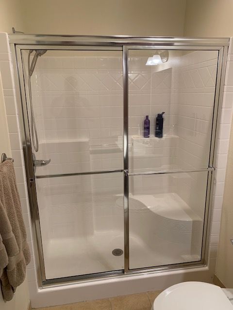 Shower stall with sliding glass doors, chrome frame, white tile walls, and a built-in seat.