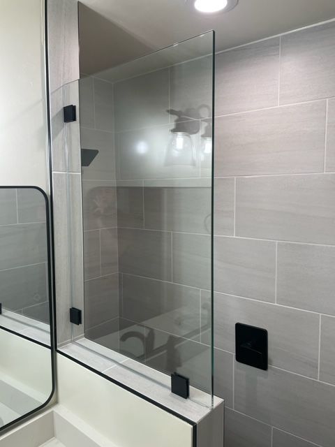 Shower with glass partition and gray tiled walls, black hardware.
