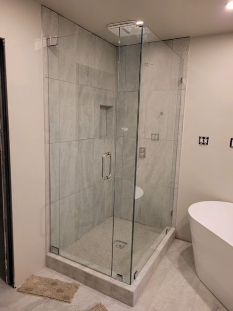 Glass shower enclosure with gray tile, a door, and a built-in shelf in a modern bathroom.
