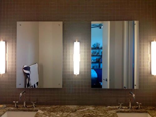 Bathroom vanity with two mirrors, sinks, and sconce lighting on a tiled wall.