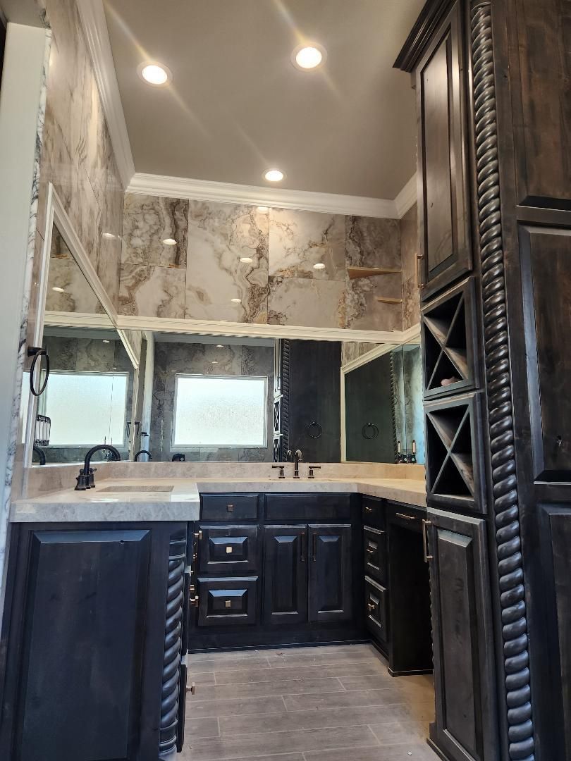 Dark wood bathroom with marble-look wall, cabinets, mirrors, and recessed lighting.