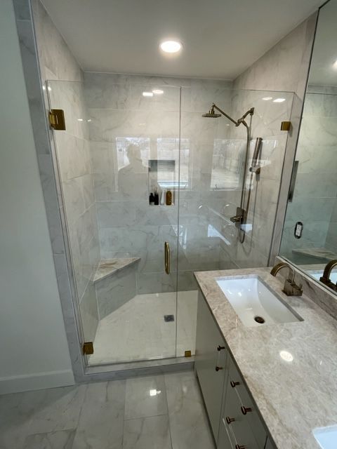 Modern bathroom with marble tile, glass shower, gold fixtures, and a vanity.