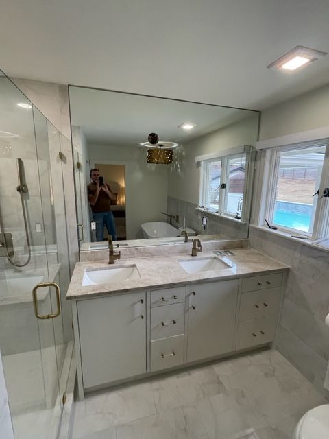 Bathroom with large mirror over double vanity, shower and windows.
