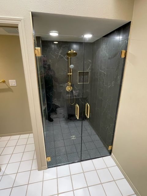 A glass shower enclosure with gold fixtures and dark gray tile.