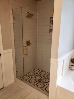 Glass-door shower with gold fixtures and geometric tile floor. White subway tile walls.