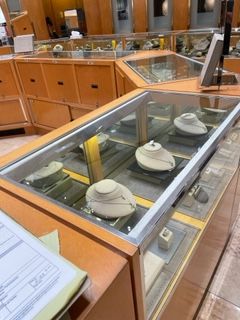Jewelry display case in a store, filled with necklaces on white busts, with wood cabinetry.