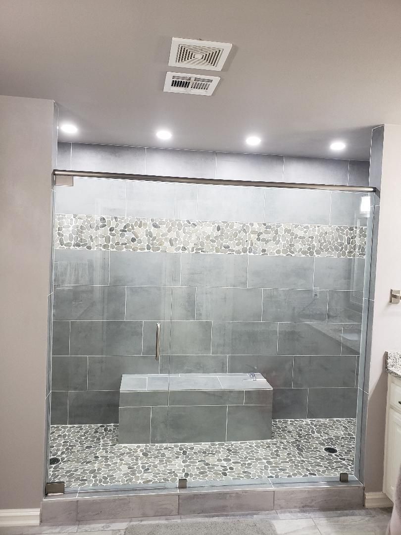 Newly tiled shower with glass door and stone accent. Gray walls, bench, and stone tile floor.