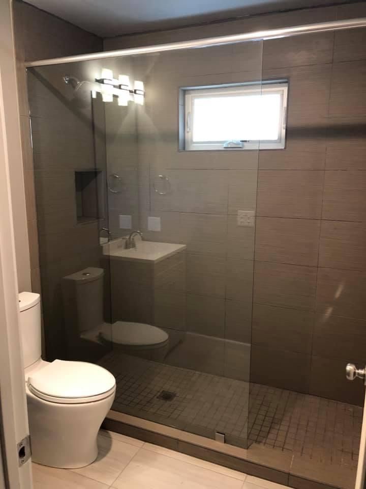 Small bathroom with shower, toilet, and sink; gray tiled walls, glass shower door.