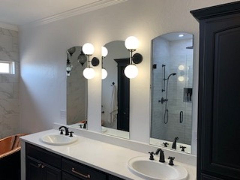Bathroom vanity with black cabinets, white countertop, arched mirrors, and globe sconces.