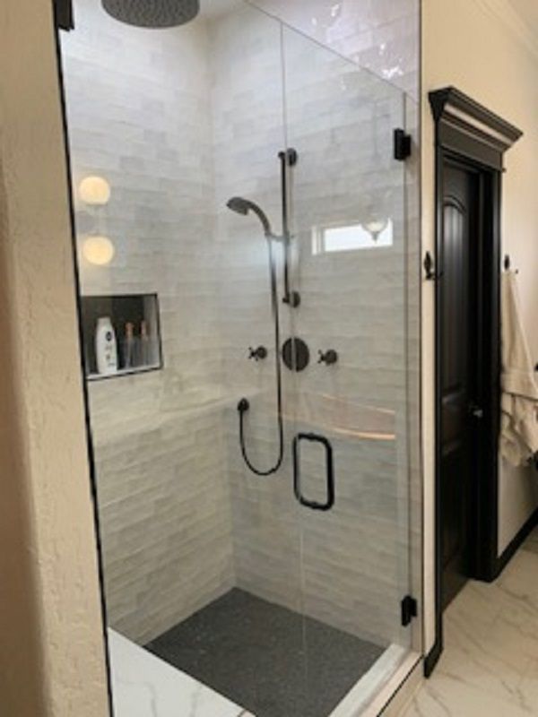 Shower with glass door, black fixtures, and white tiled walls. Dark gray floor and recessed shelf for toiletries.