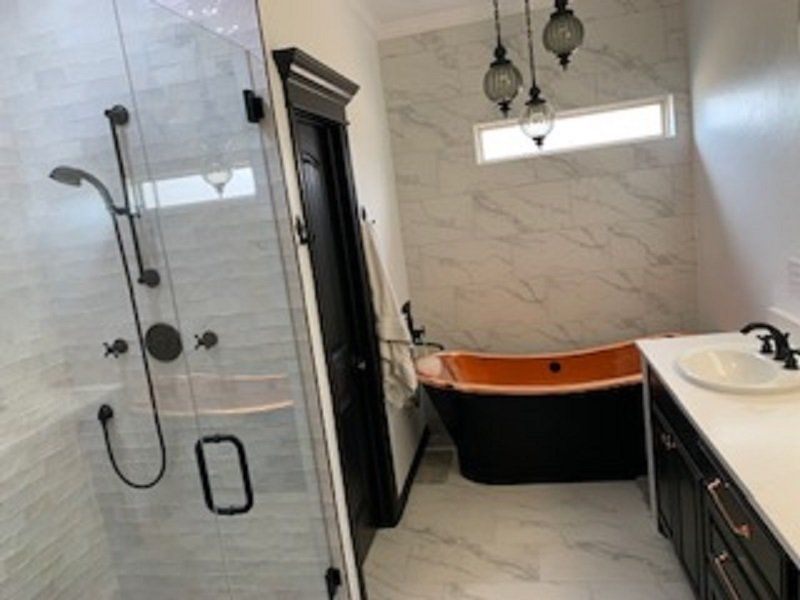 Bathroom with a black tub and vanity, marble-look tiles, glass shower, and bronze fixtures.