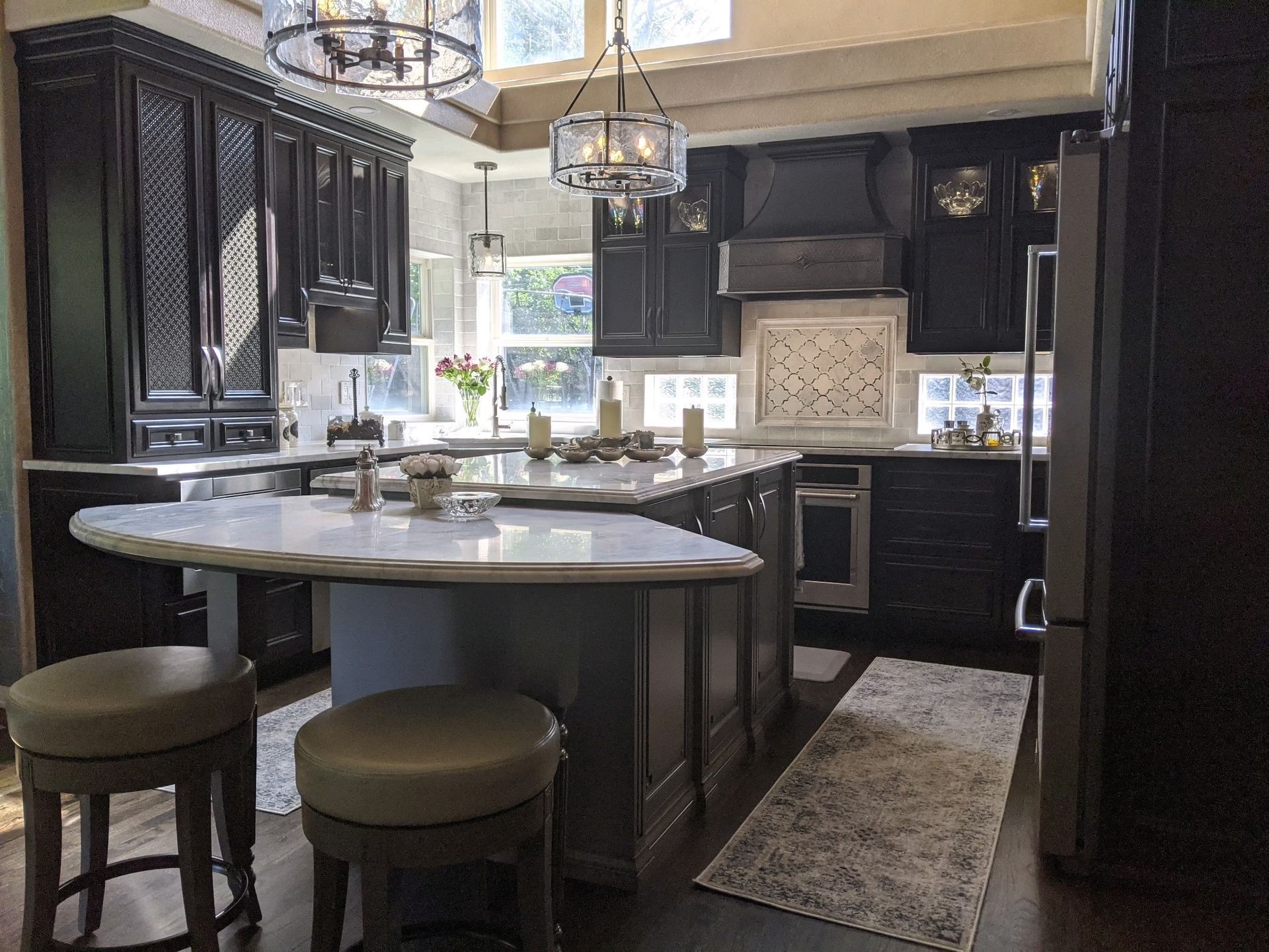 A kitchen with black cabinets and stools and a large island in the middle.