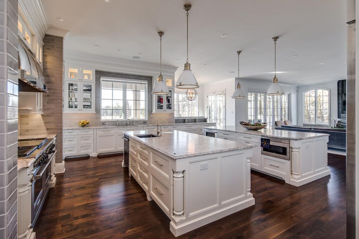 A large kitchen with white cabinets , granite counter tops , stainless steel appliances and hardwood floors.