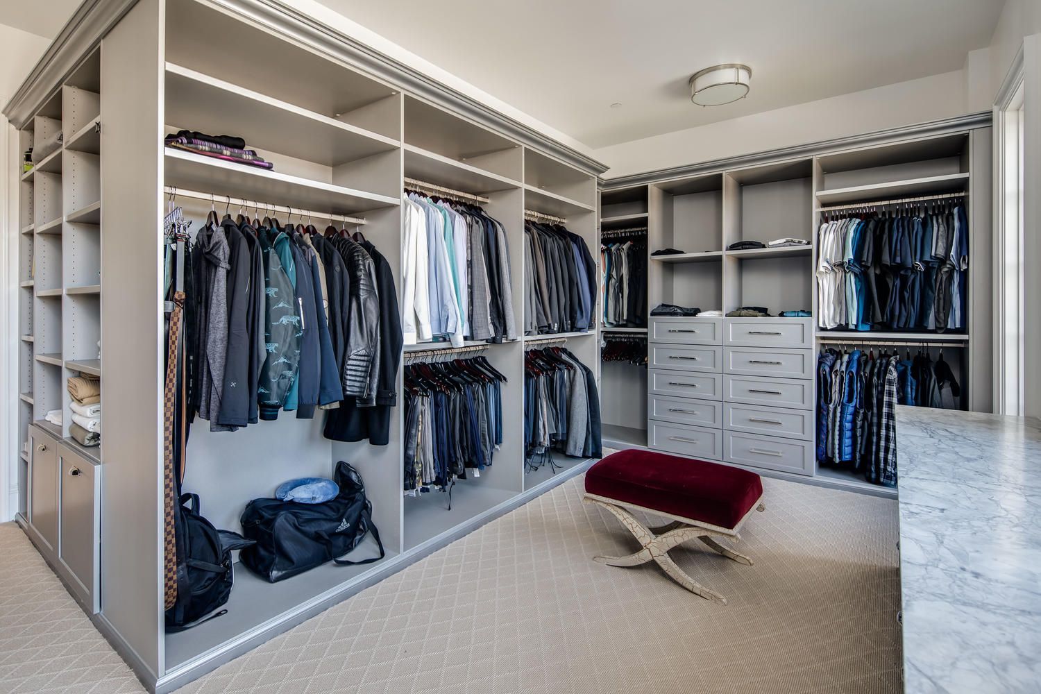 A walk in closet filled with lots of clothes and a red ottoman.