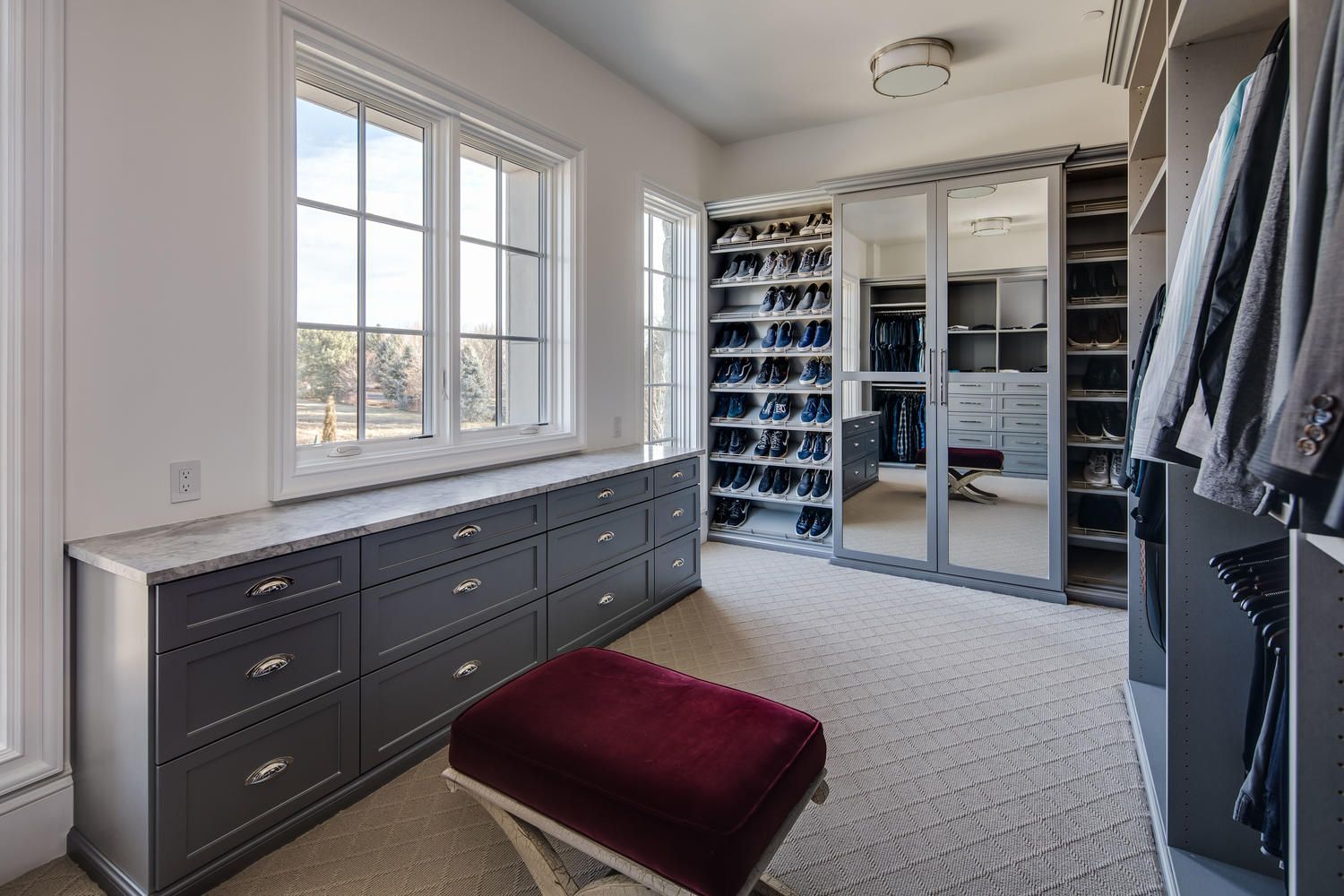 A walk in closet with a red ottoman and a large window.