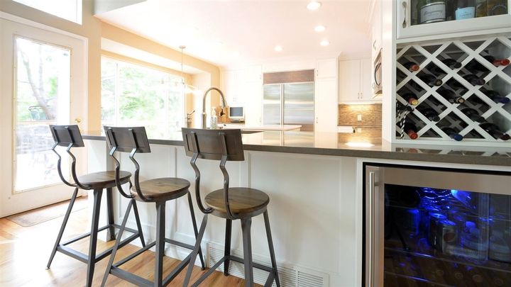 A kitchen with three bar stools and a wine cooler.