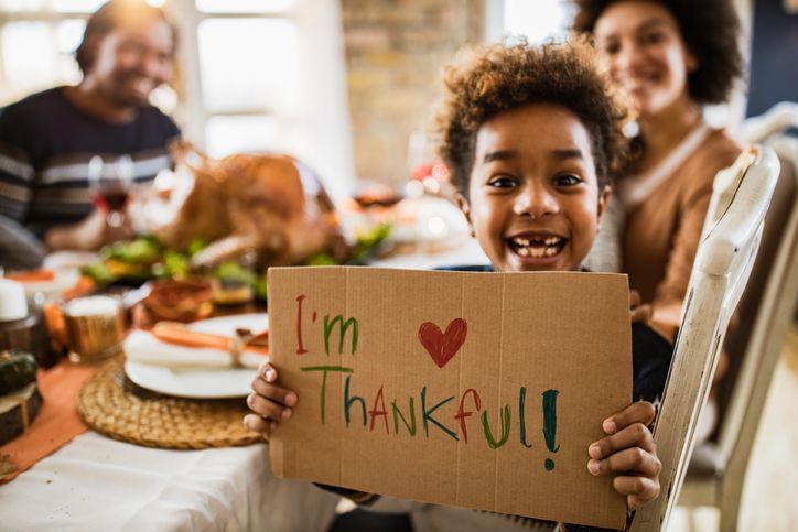 A young boy is holding a cardboard sign that says `` i 'm thankful ''.
