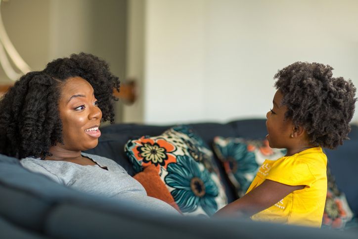 A woman and a child are sitting on a couch talking to each other.