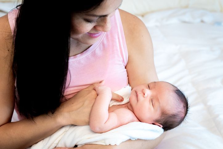 A woman is holding a newborn baby in her arms on a bed.