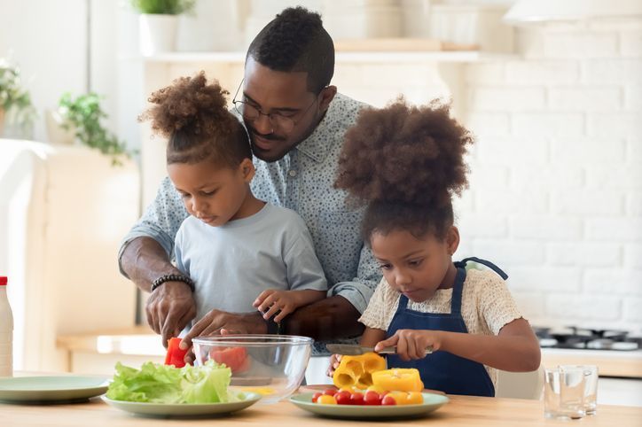 A man and two children are preparing food in a kitchen.