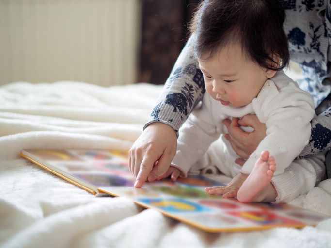 A woman is reading a book to her baby on a bed.
