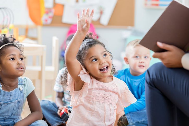 A little girl is raising her hand to answer a question in a classroom.