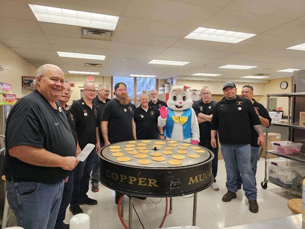 A group of men are standing around a table with a mascot on it.
