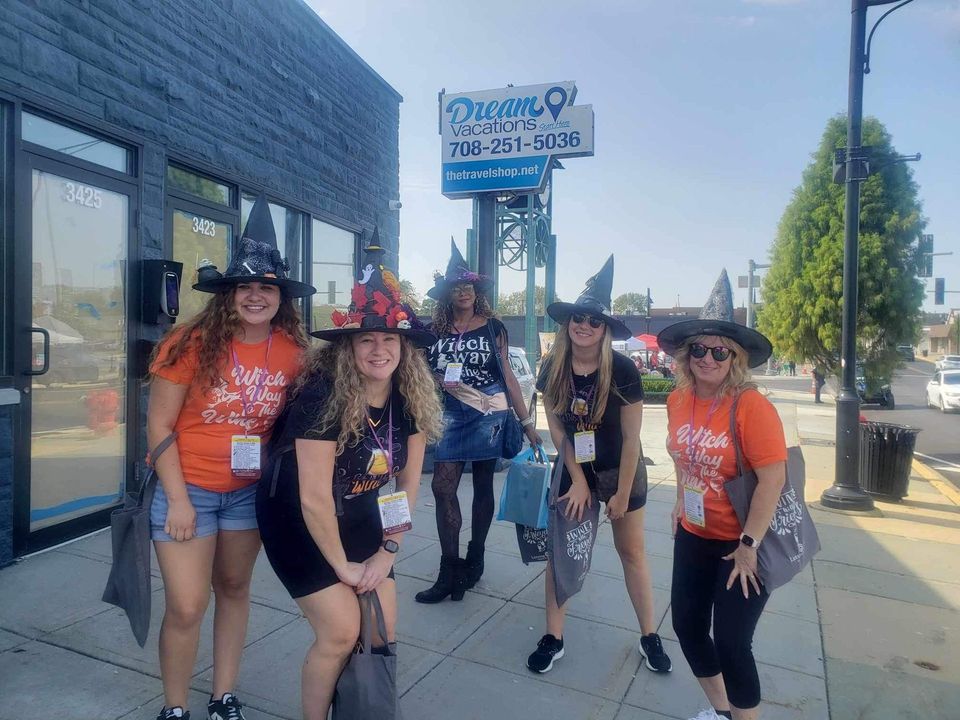 A group of women dressed as witches are standing on a sidewalk in front of a building.