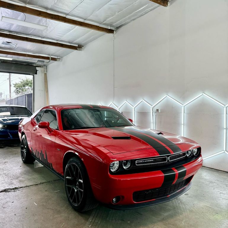 Red Dodge Challenger with black racing stripes and a custom city skyline decal, displayed indoors, showcasing car ceramic coating service