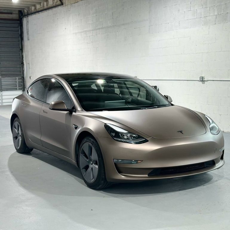 Matte bronze-wrapped Tesla Model 3 inside a garage, showcasing a custom vehicle wrap service in Los Angeles, CA