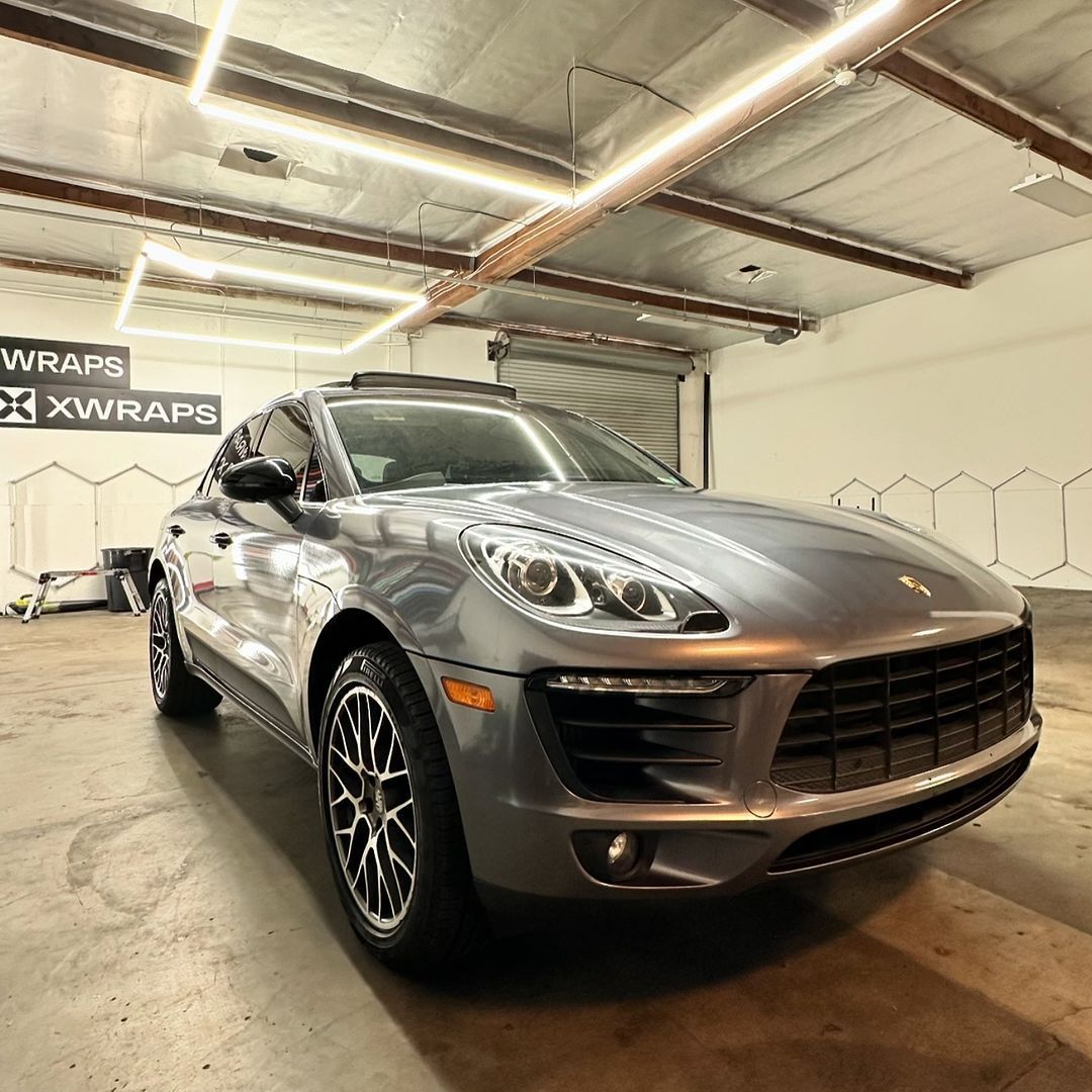 Sleek Porsche Macan with window tinting and car wraps by XWRAPS Los Angeles, showcasing luxury automotive transformation in high-end workshop