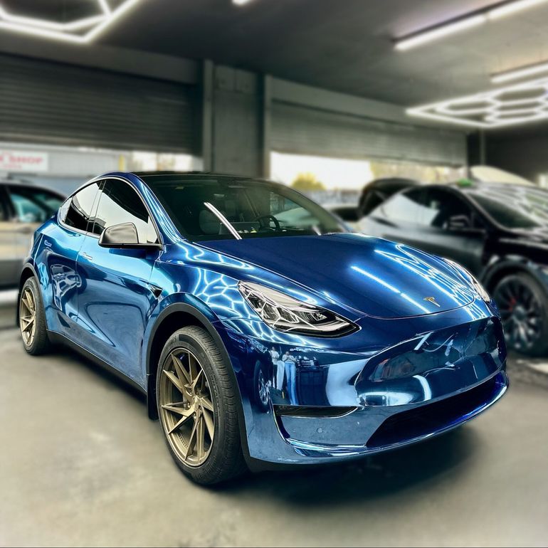 A Tesla Model Y with a glowing blue car wrap parked indoors, showcased alongside other custom car wraps at XWRAPS in Los Angeles