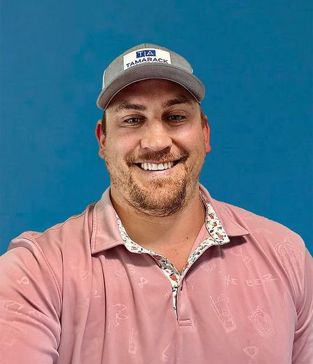 Agent Brandon is wearing a baseball hat and a pink shirt and smiling for the camera.