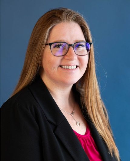 Agent Lisa is wearing glasses and a black jacket and smiling for the camera.
