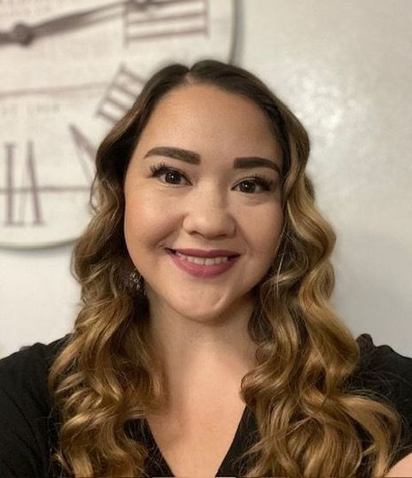 Assistant Mikayla has long hair and is smiling in front of a clock.