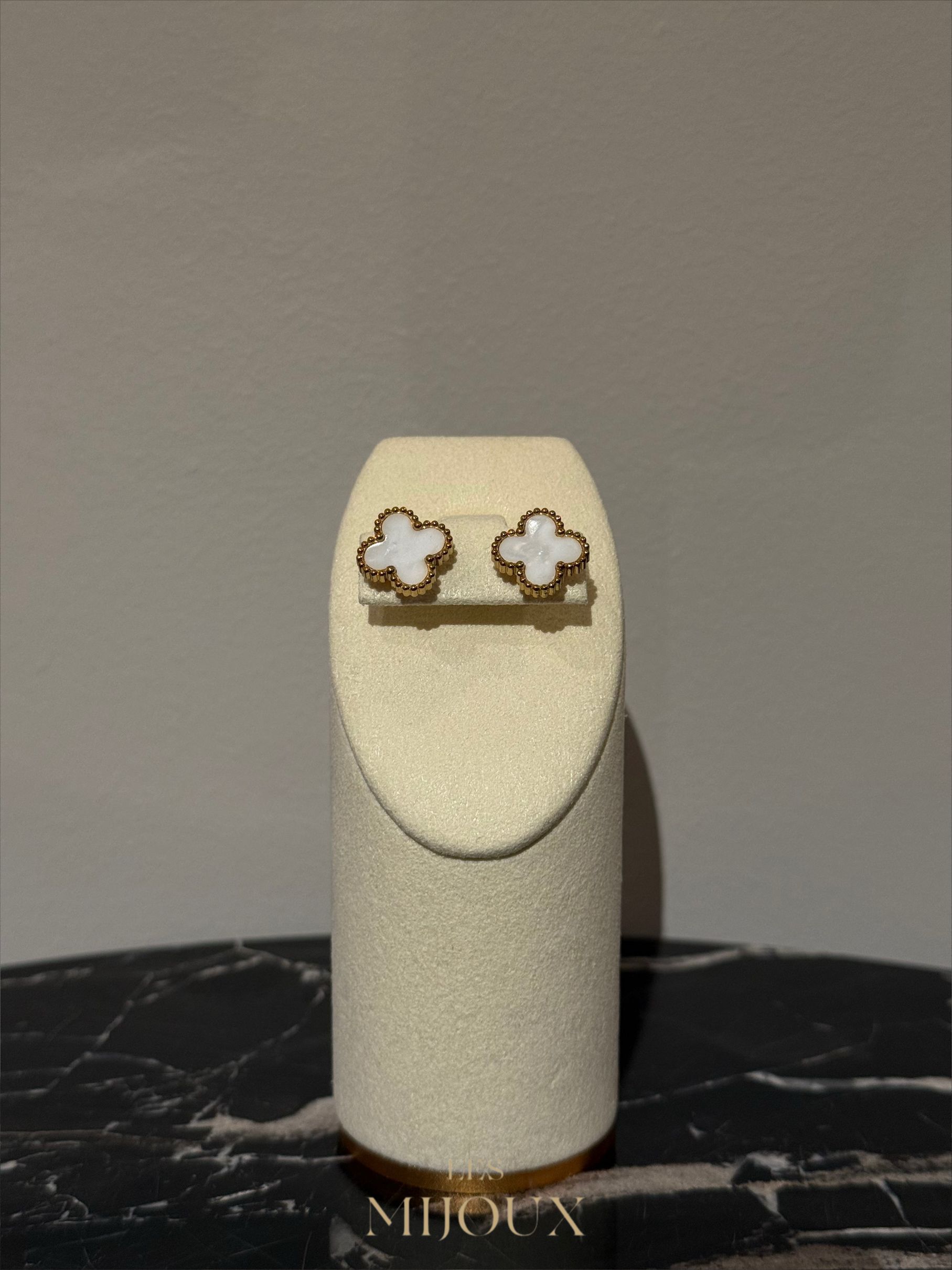 Wolkvormige oorknopjes, wit en goud, op een displaystandaard met een marmeren en neutrale achtergrond.