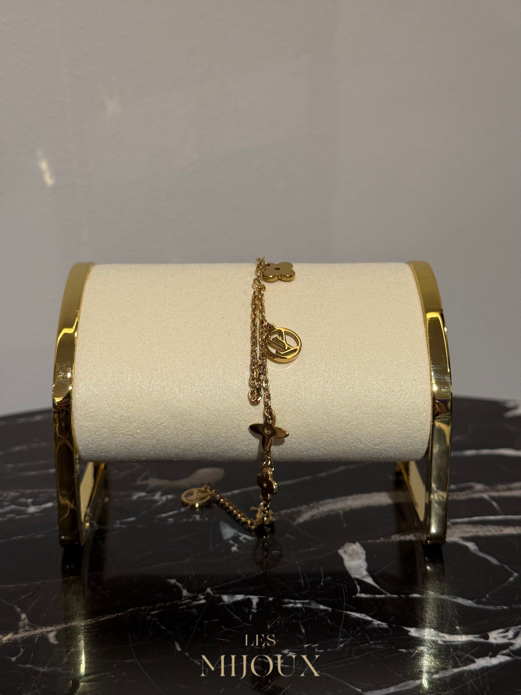 Gouden armband met bedeltjes op een displaystandaard, met een marmeren oppervlak.