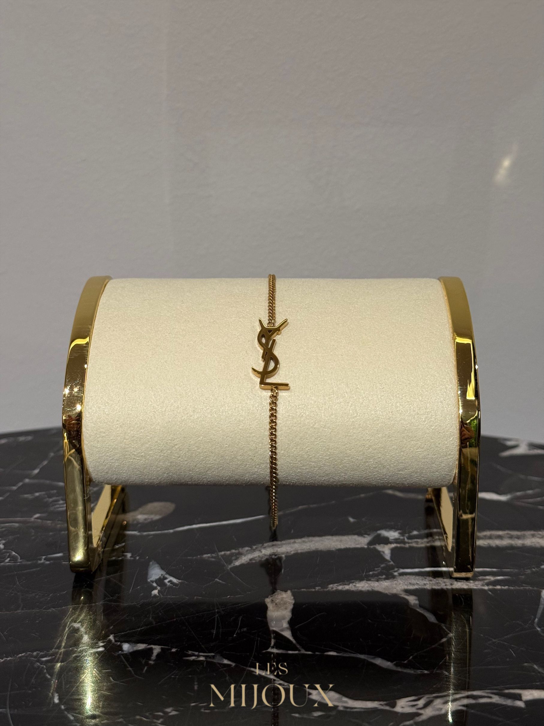 Armband met een gouden YSL-logo op een witte cilinder met gouden rand.