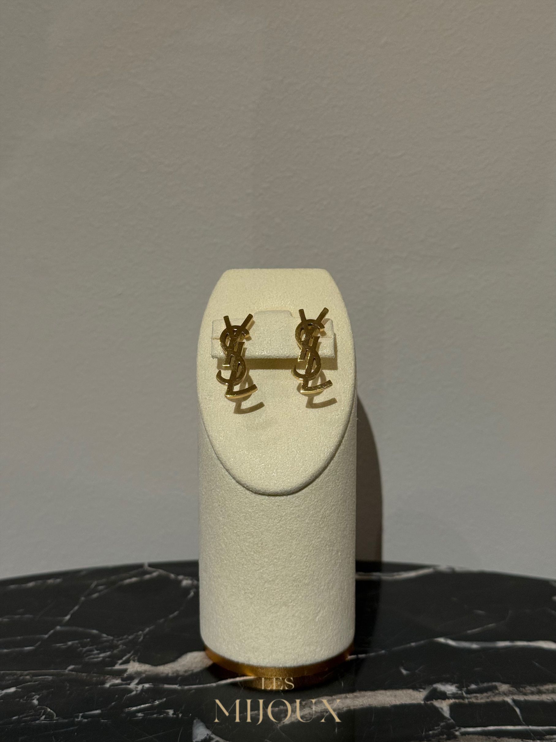 Goudkleurige oorbellen op een glinsterende witte displaystandaard op een marmeren ondergrond.