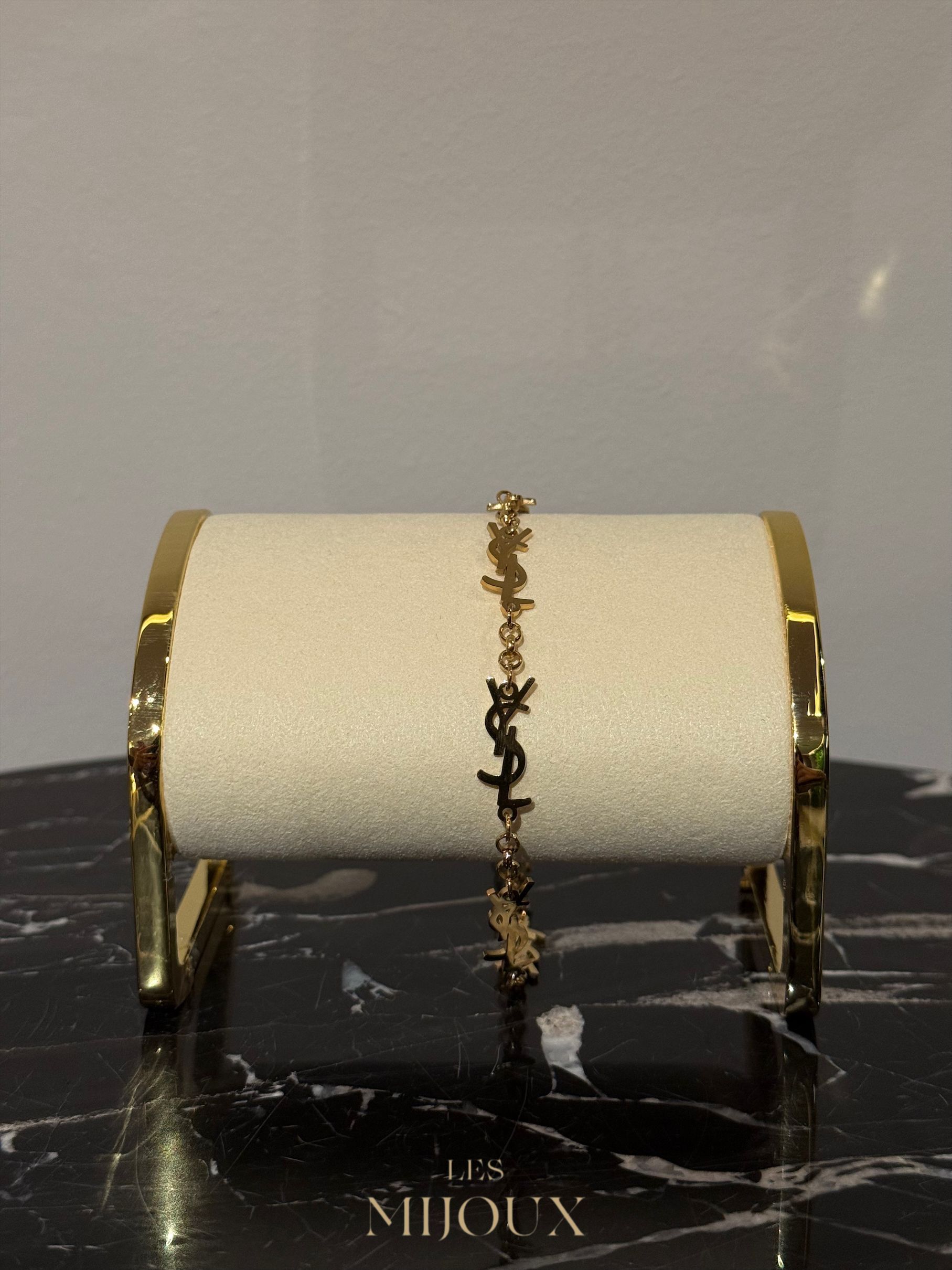Gouden Saint Laurent-armband tentoongesteld op een crèmekleurige standaard met een zwarte marmeren voet.