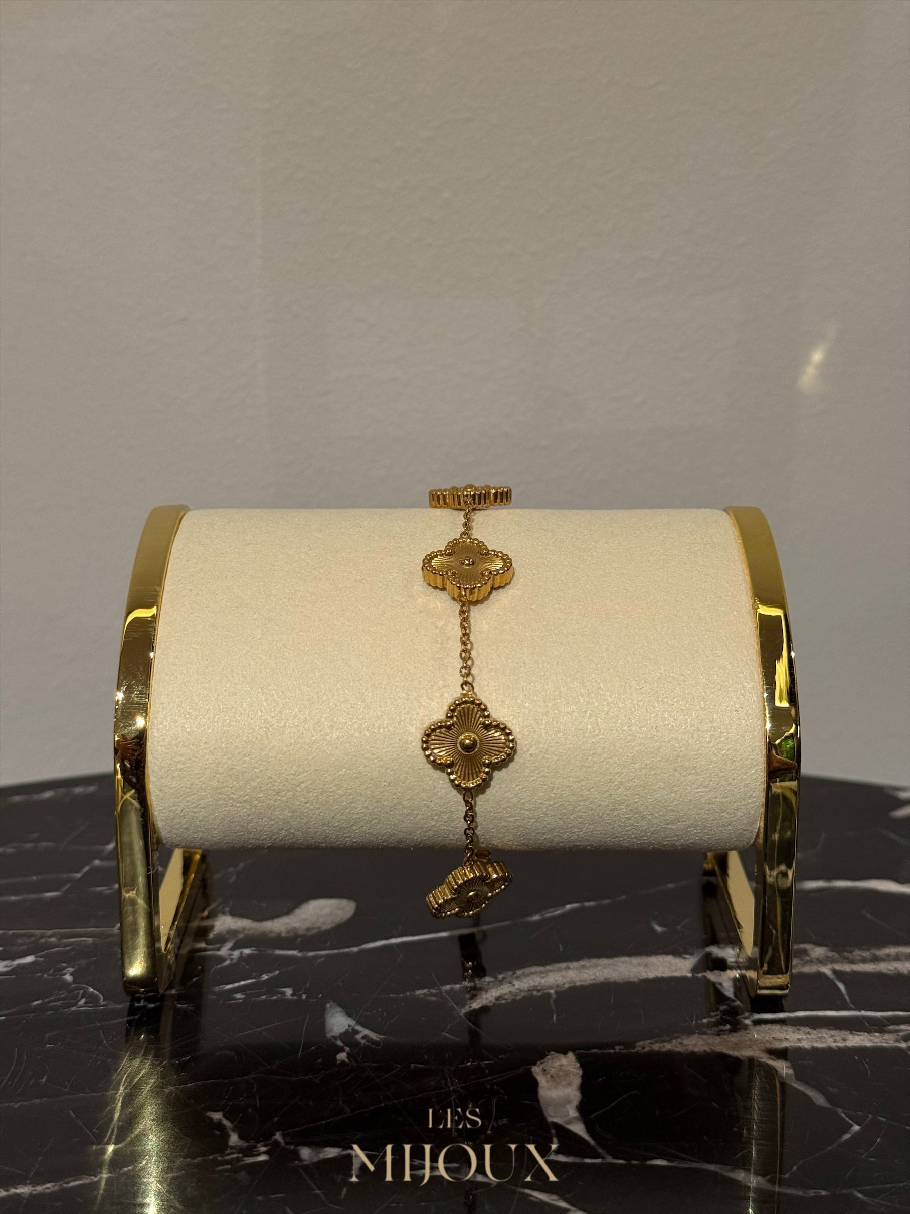 Gouden klaverarmband op een crèmekleurige displaystandaard met gouden rand, geplaatst op marmer.