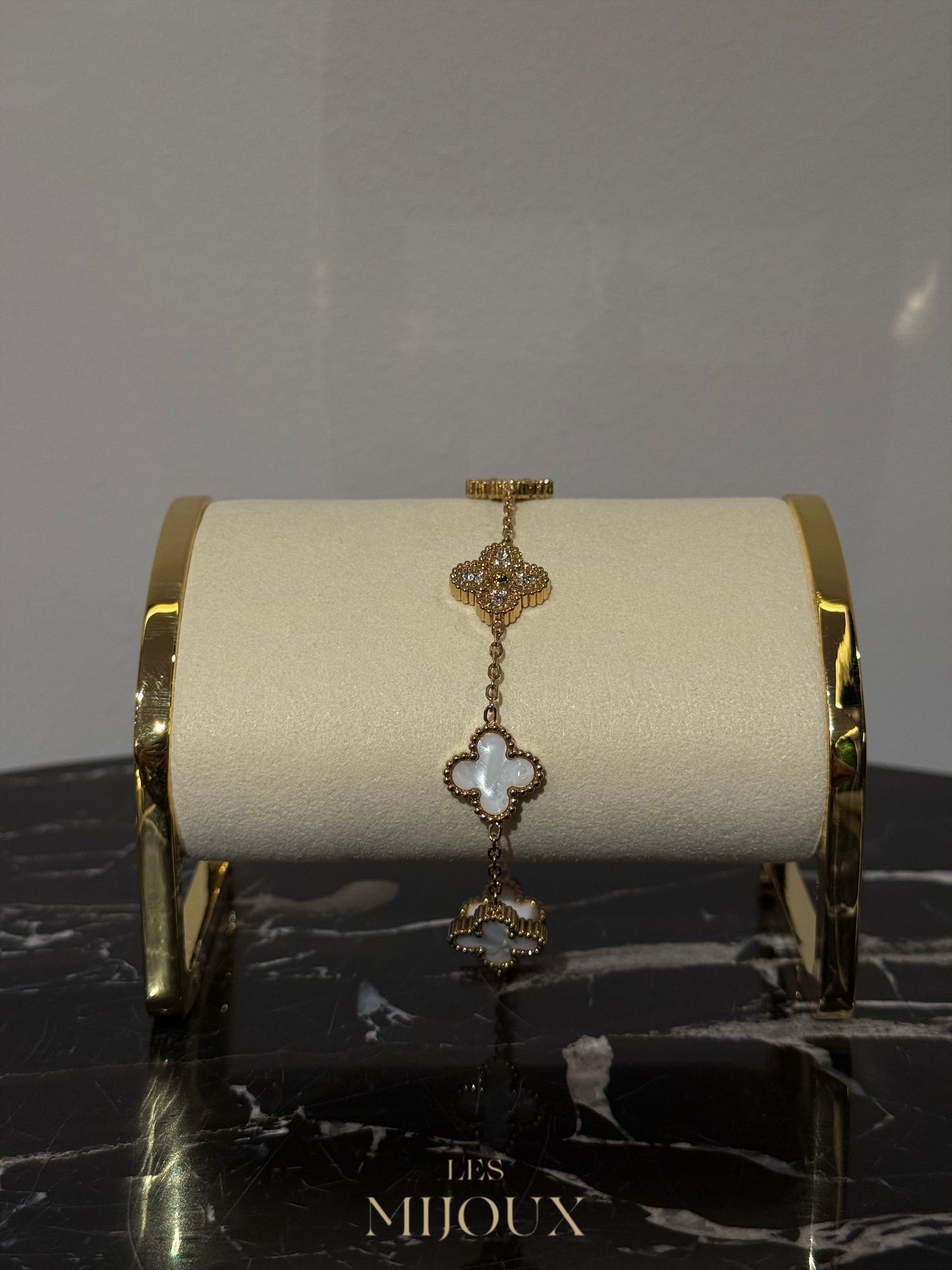 Gouden armband met klavermotieven, tentoongesteld op een crèmekleurige standaard met een marmeren voet.