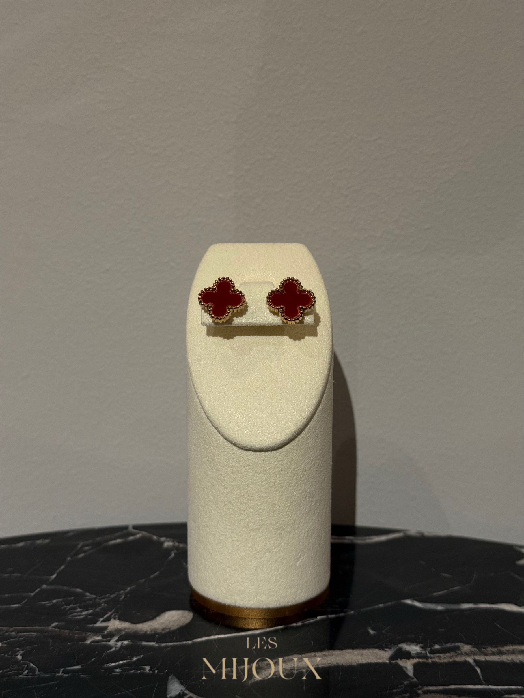 Oorbellen in de vorm van een rode klaver op een witte displaystandaard, die rust op een zwart gemarmerd oppervlak.