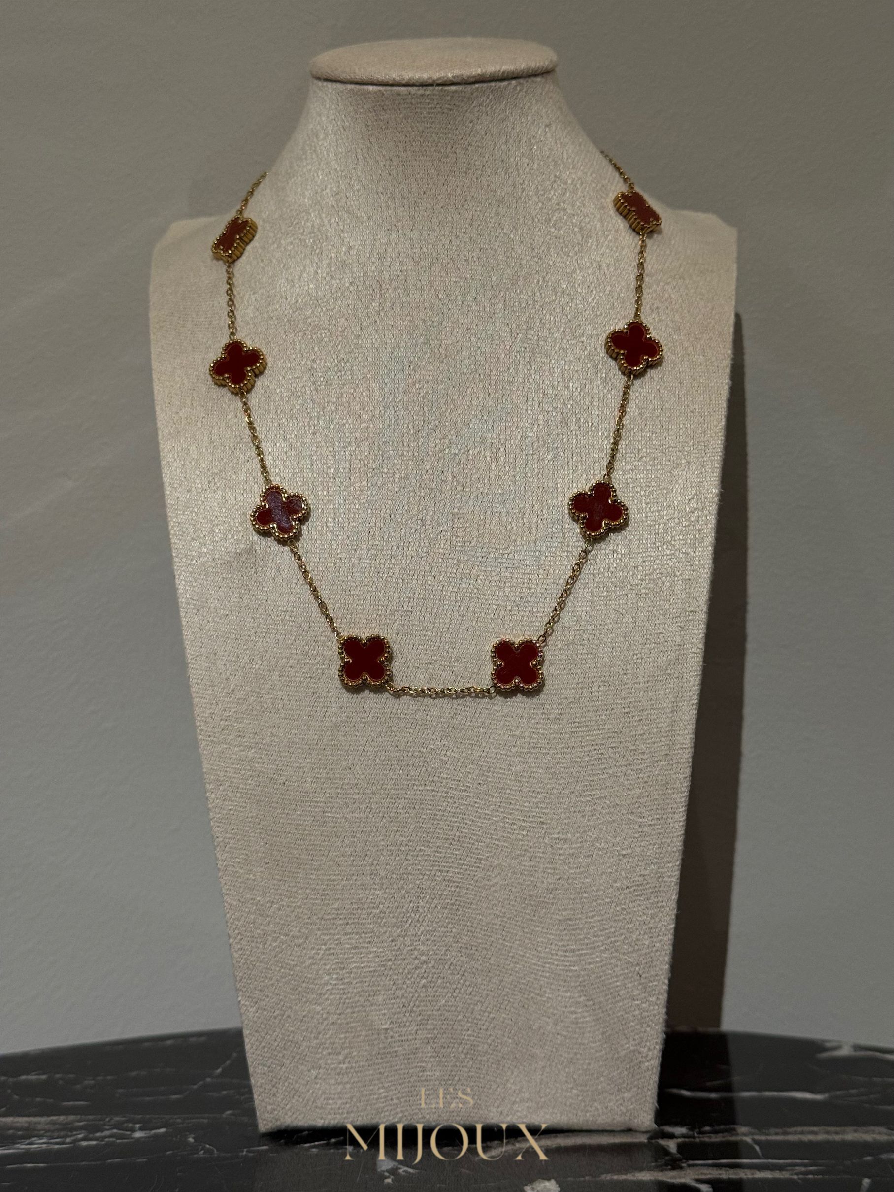 Gouden halsketting met rode klavervormige hangers op een paspop.