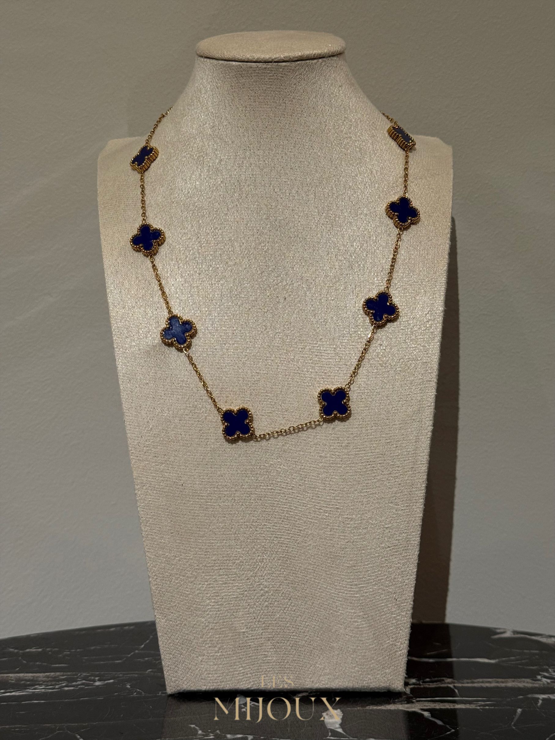 Gouden halsketting met donkerblauwe klavervormige hangers op een neutrale displaystandaard.