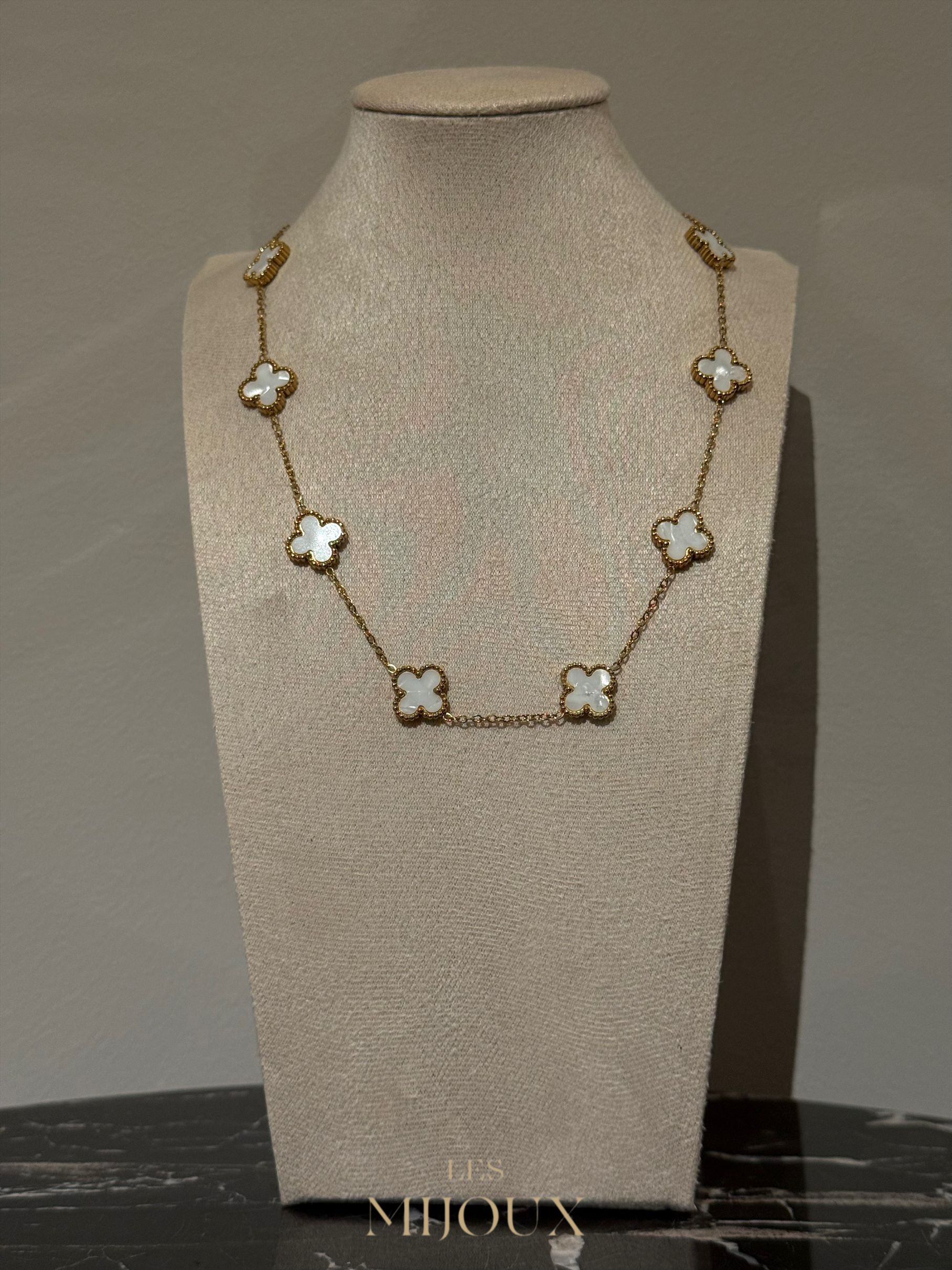 Gouden halsketting met klavervormige hangers, tentoongesteld op een beige sieradenbuste.